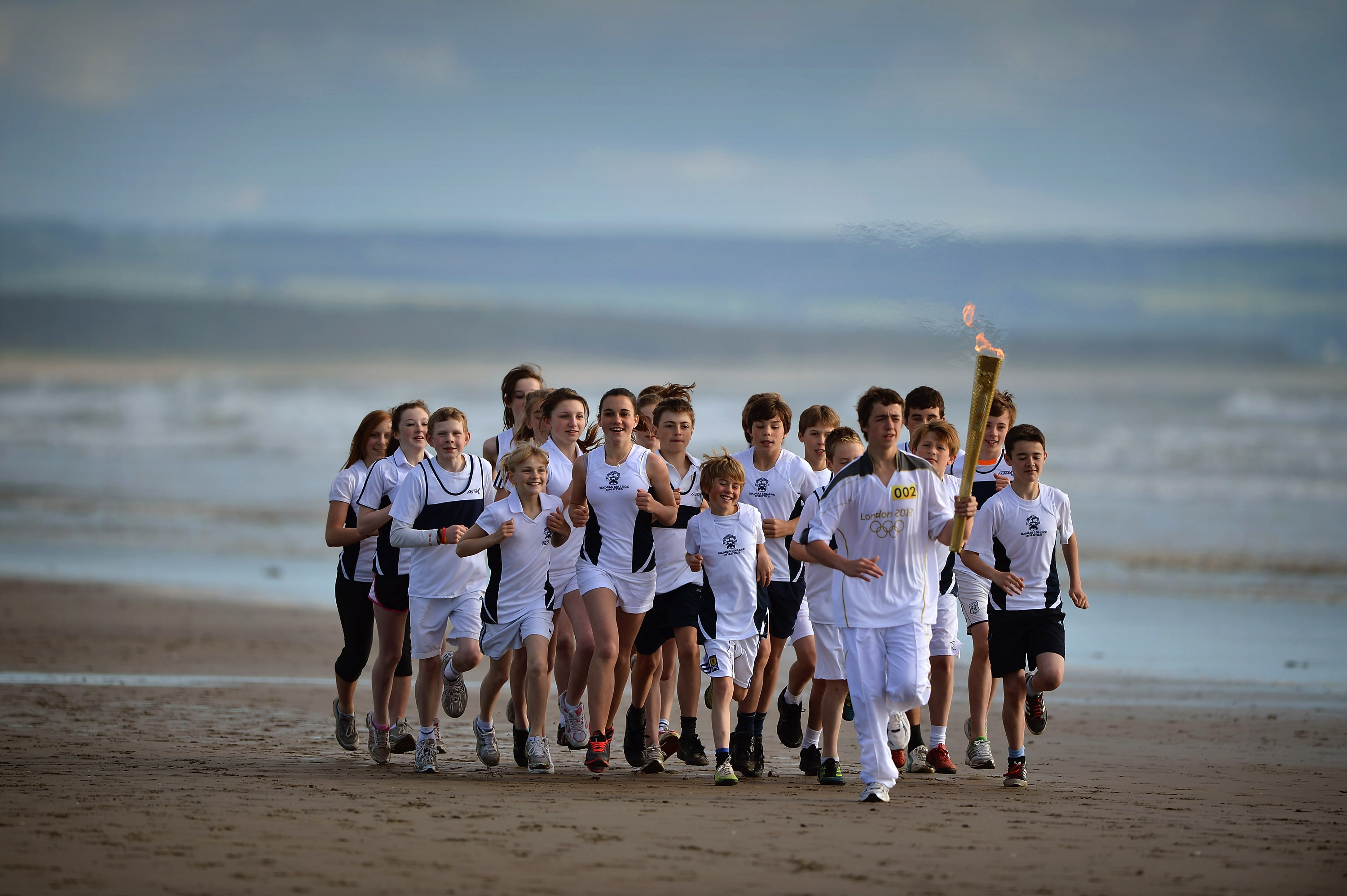 Un groupe d'enfant courent avec la torche olympique sur la plage
